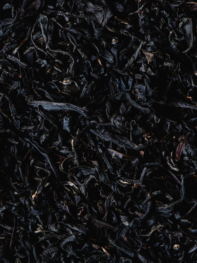 Dark twisted oolong strips with reddish edges beside a cup of amber liquor